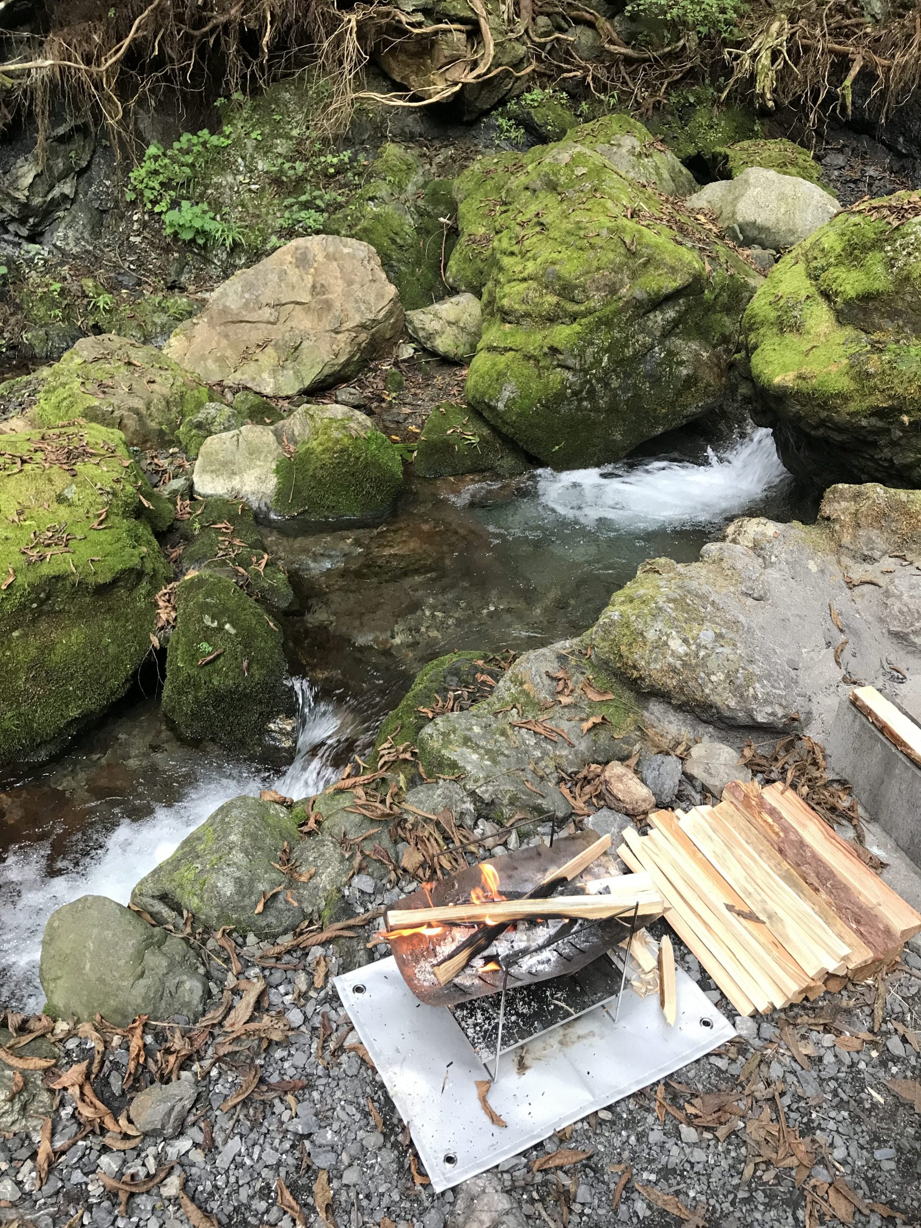 渓流を前に焚き火台で薪を燃やす